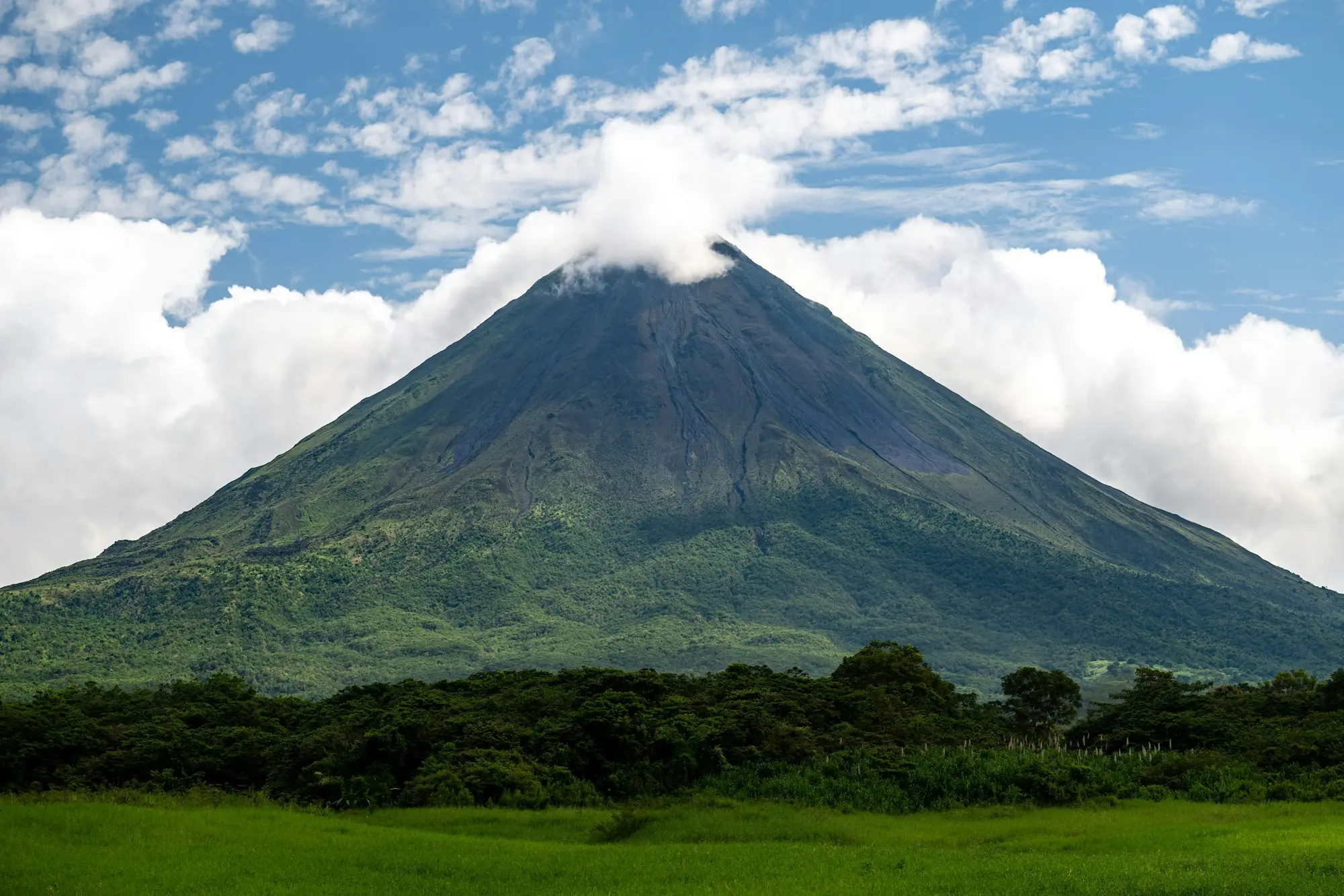 Arenal volcano's green cone rising above forest under a partly cloudy sky