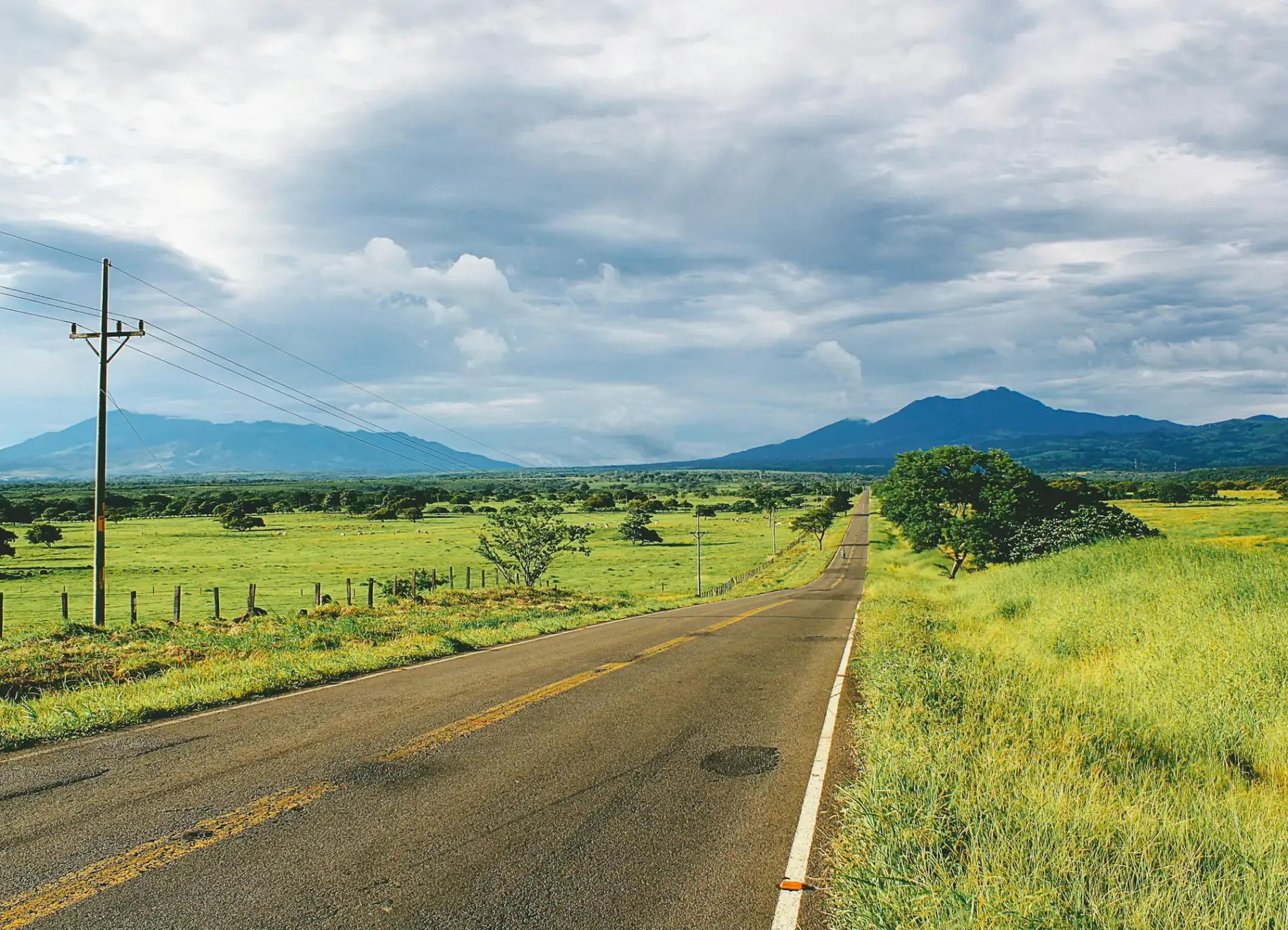 A paved highway leading toward green mountains through the Costa Rica countryside
