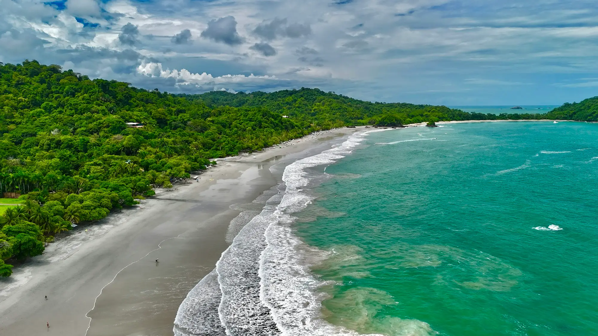 Aerial view of a long sandy Pacific beach in Costa Rica with white surf and forested hills behind