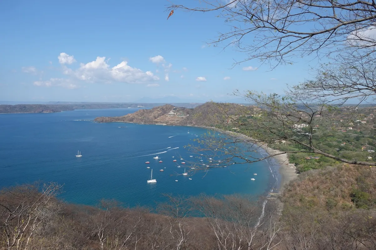Calm horseshoe bay with sailboats anchored below dry-forest hills at Playas del Coco in Guanacaste, Costa Rica