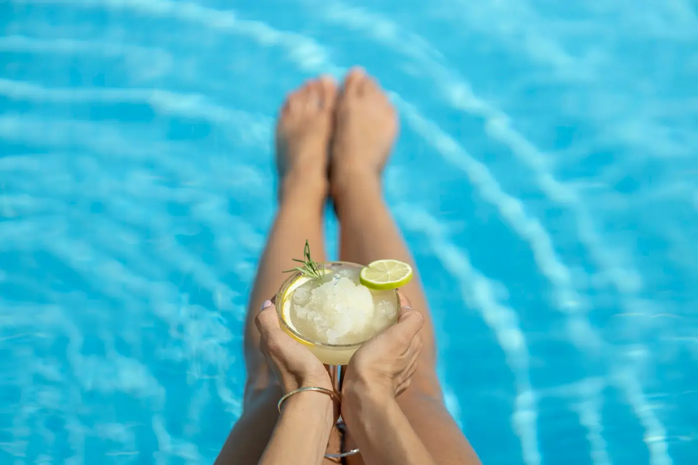 A guest holding a frozen cocktail with lime over the edge of a resort pool