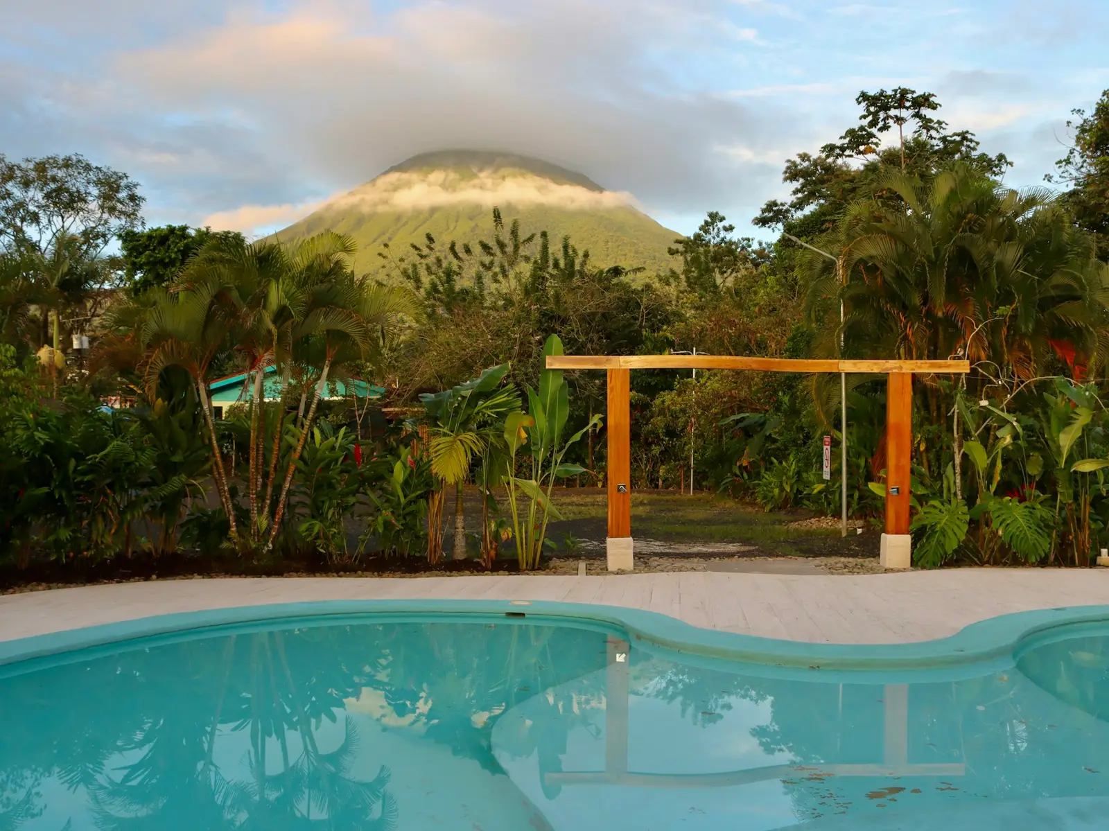 A pool framed by palms and tropical plants with Arenal volcano rising behind