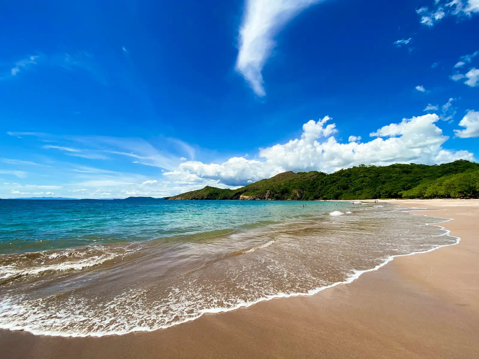 A wide sandy Guanacaste beach with gentle surf and a forested headland