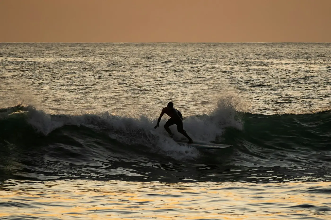 A surfer riding a small wave at sunset on Costa Rica's Pacific coast