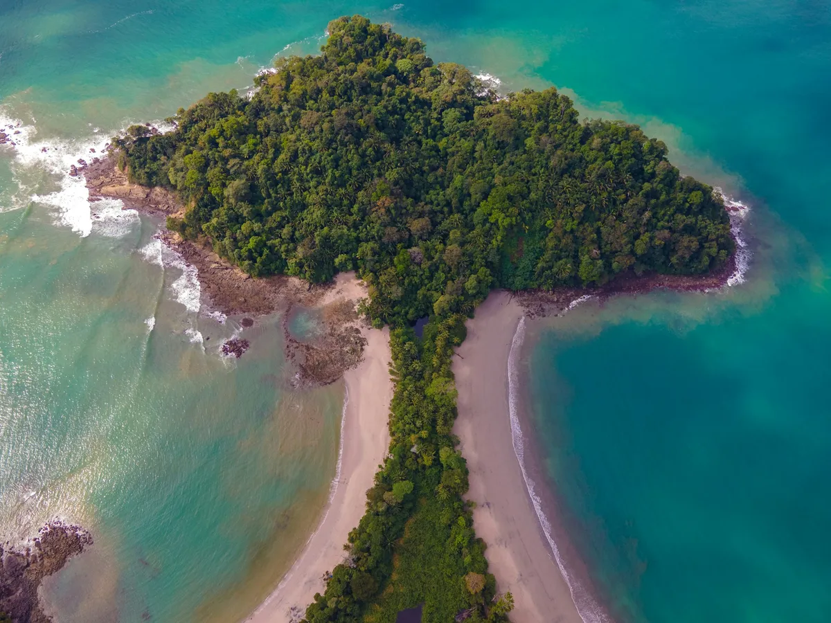 Aerial view of a rainforest-covered point and white-sand beach ringed by turquoise Pacific water on Costa Rica's South Pacific coast
